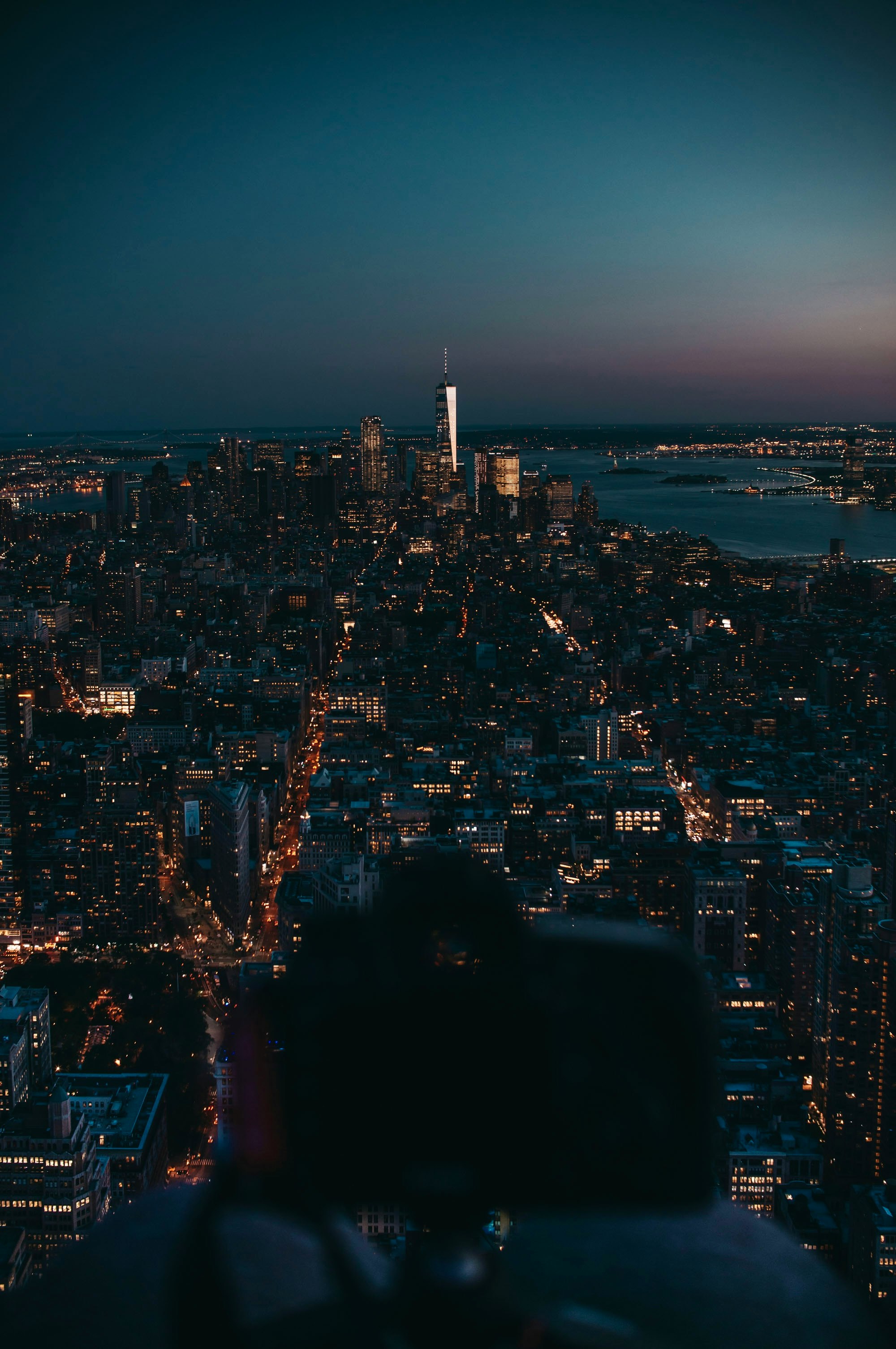 man sitting on the edge of a building looking at the city lights during night time